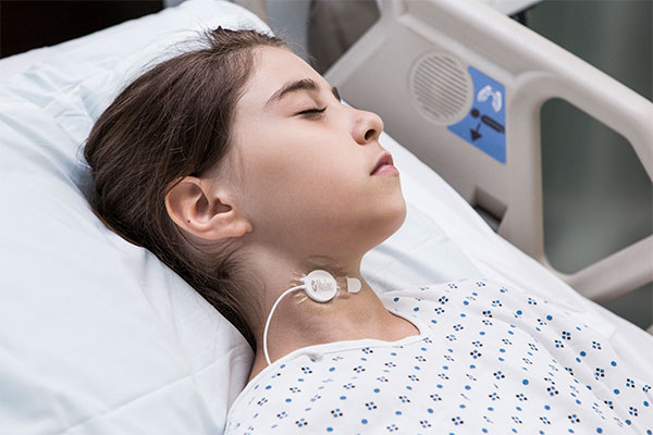 Masimo – Enfant qui porte un capteur de fréquence respiratoire acoustique (RRa) sur le cou dans son lit d’hôpital